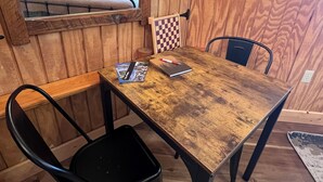 Una mesa de madera para comer con dos sillas negras, un juego de mesa a cuadros, una computadora portátil y una revista.