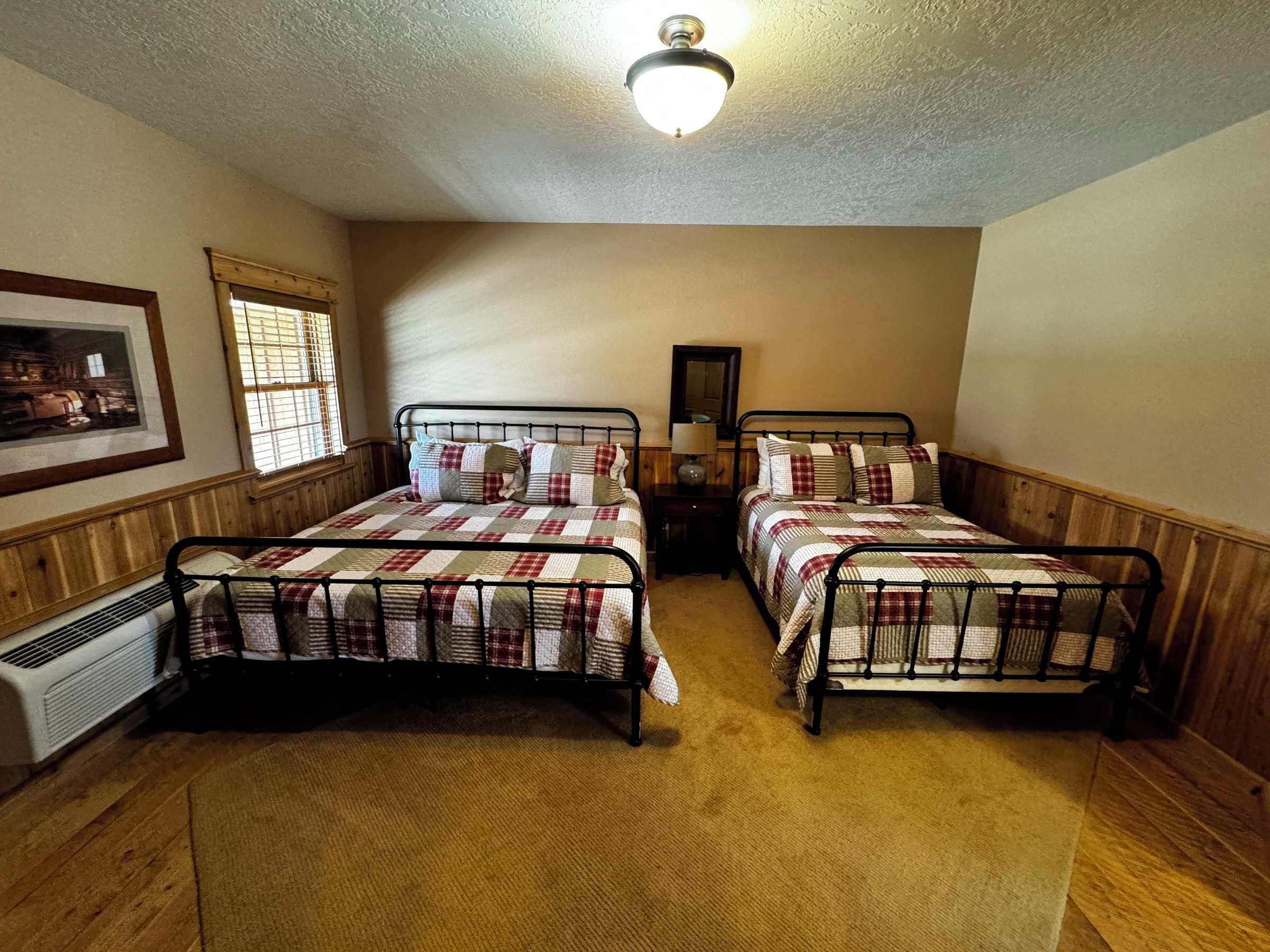 A room with two metal bunk beds, a ceiling fan, a framed picture on the wall, and a window with blinds.