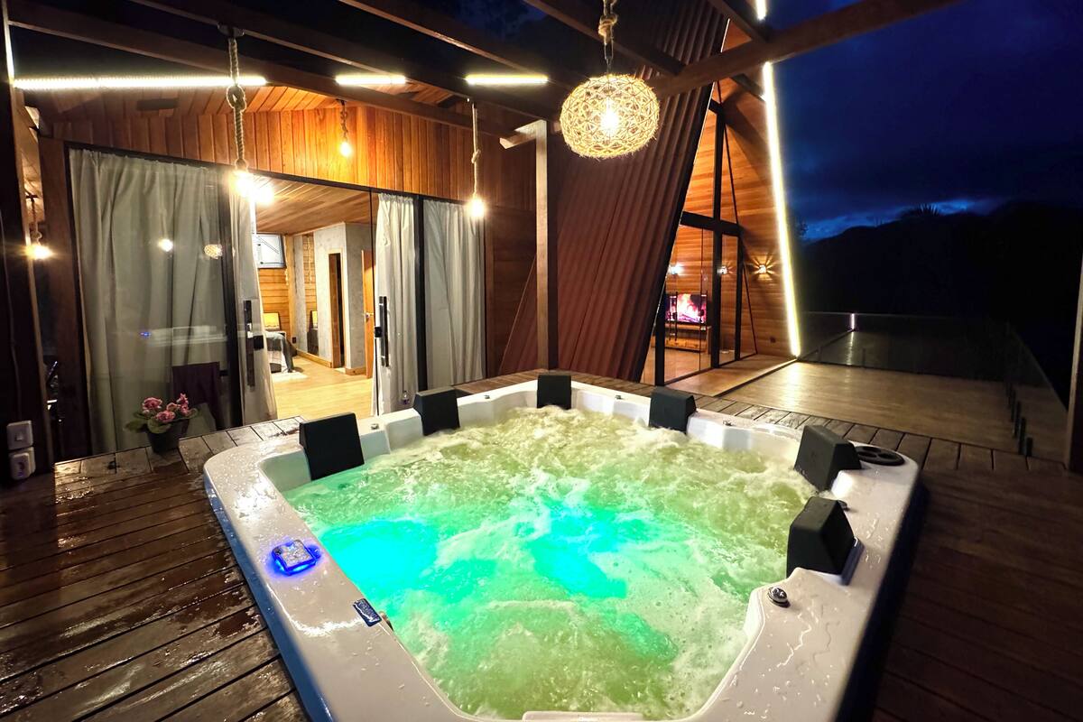 Un bain à remous avec un éclairage bleu, une terrasse en bois et une vue sur un bâtiment dont les fenêtres sont dotées de rideaux.