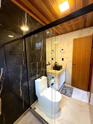 A modern bathroom with a glass-enclosed shower, a white toilet, and a wooden vanity with a sink. - Chalé com Jacuzzi a 8km de Santa Teresa (Santa Teresa)