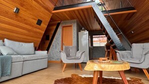 Ein modernes Loft mit Holzbalken an der Decke, einer Couch, zwei Sesseln, einem runden Holztisch und einem Fellteppich.
