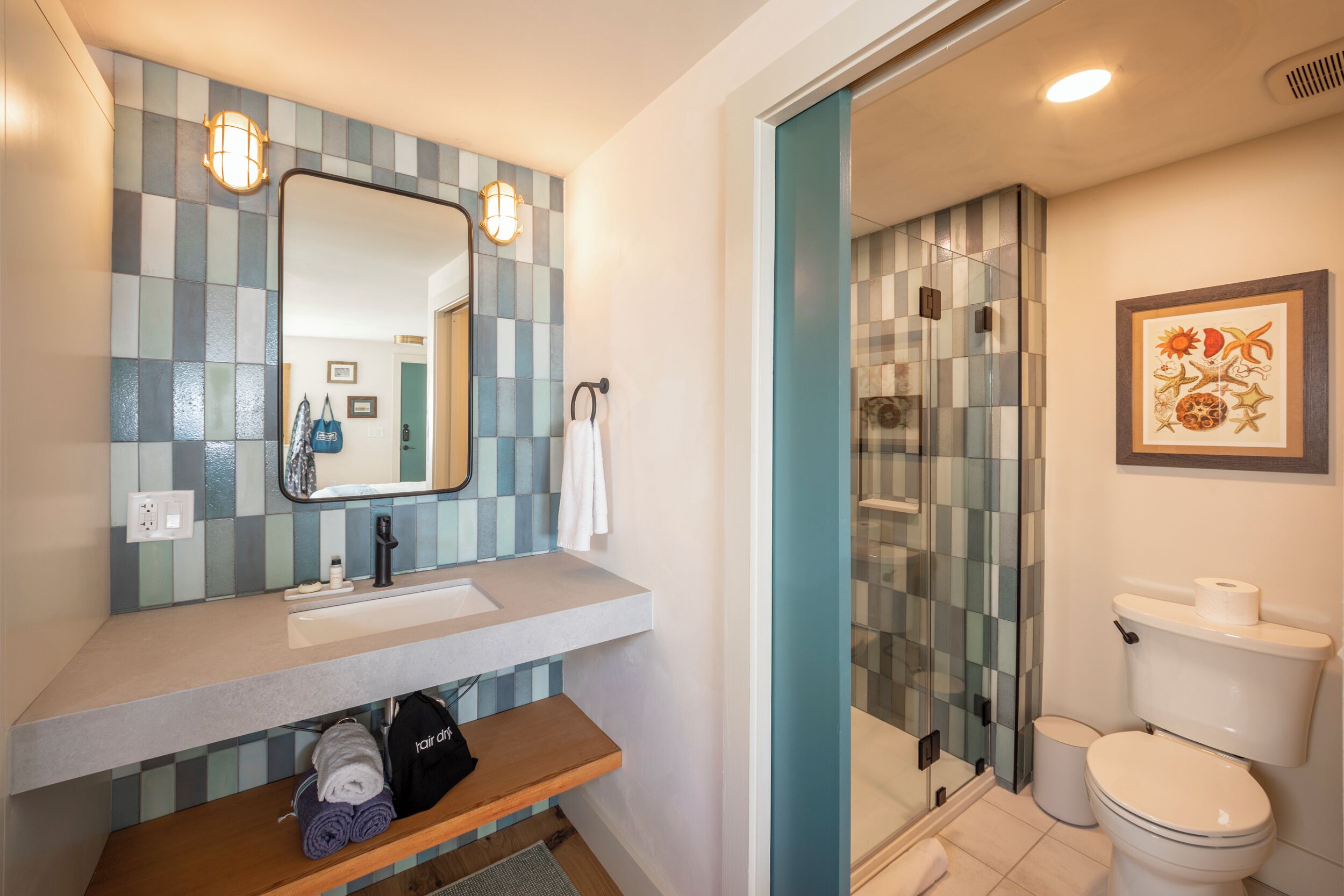 A bathroom with a mirror, sink, and toilet. There is a shower area with glass doors and a towel rack.