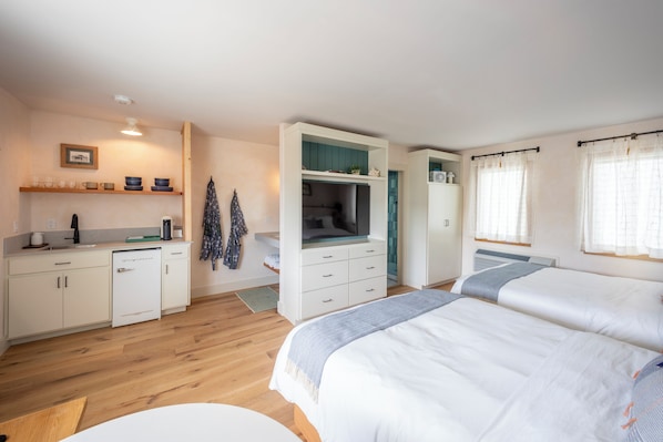 A modern bedroom with two beds, a built-in wardrobe, a small kitchenette, and a bathroom.