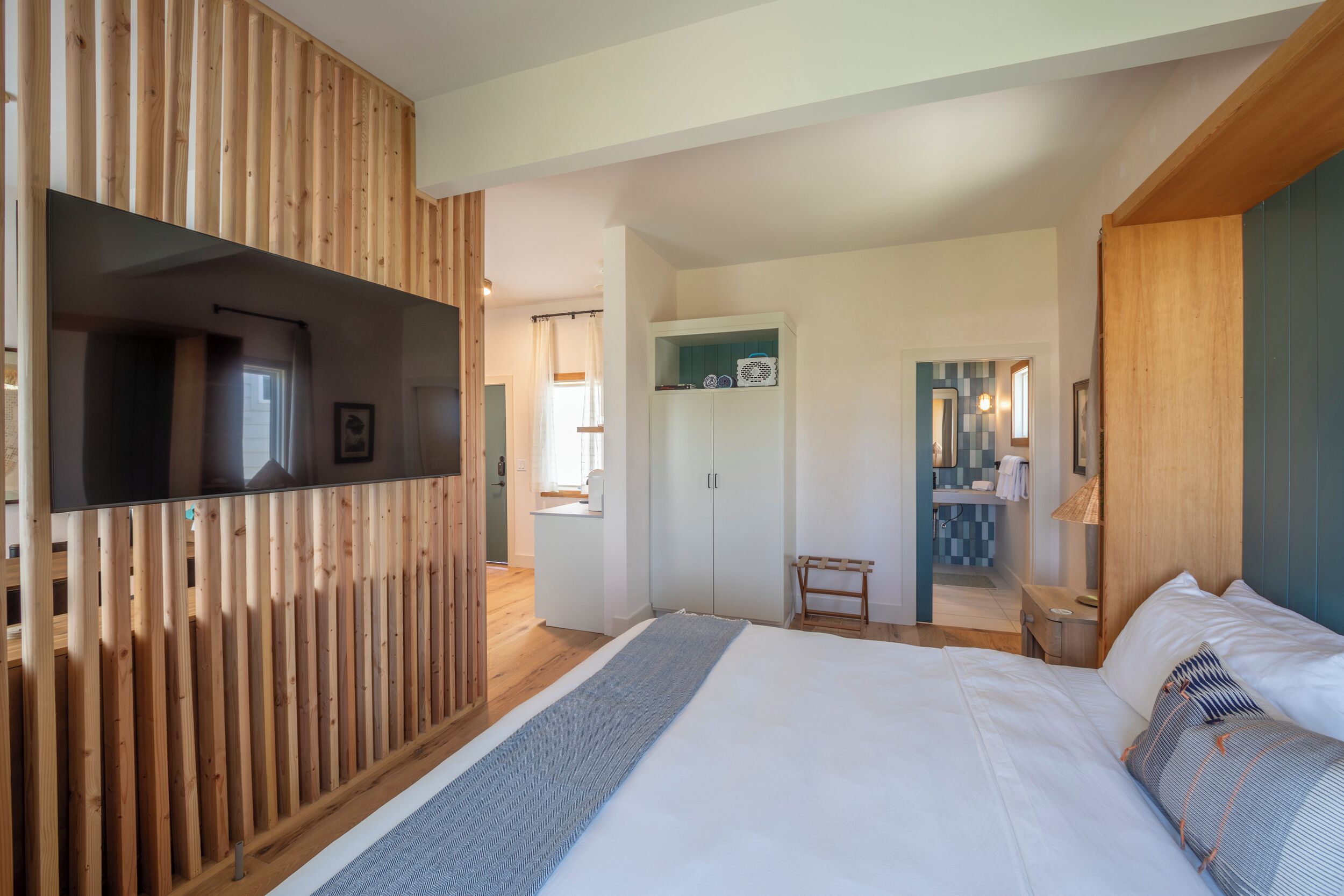 A modern hotel room with a large bed, wooden paneling, a television, and a bathroom visible through an open door.