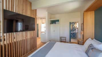 A modern hotel room with a large bed, wooden paneling, a television, and a bathroom visible through an open door.