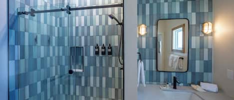 Un baño moderno con ducha de vidrio, una bañera blanca y un lavamanos con espejo.