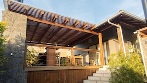 A modern house with a wooden deck, stone walls, and a staircase leading to a covered porch. - Casas Valley Boutique - Praia do Rosa (Imbituba)