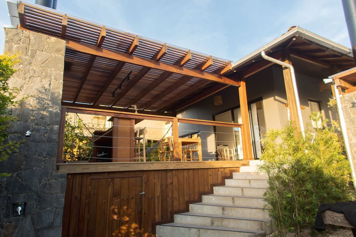 A modern house with a wooden deck, stone walls, and a staircase leading to a covered porch.
