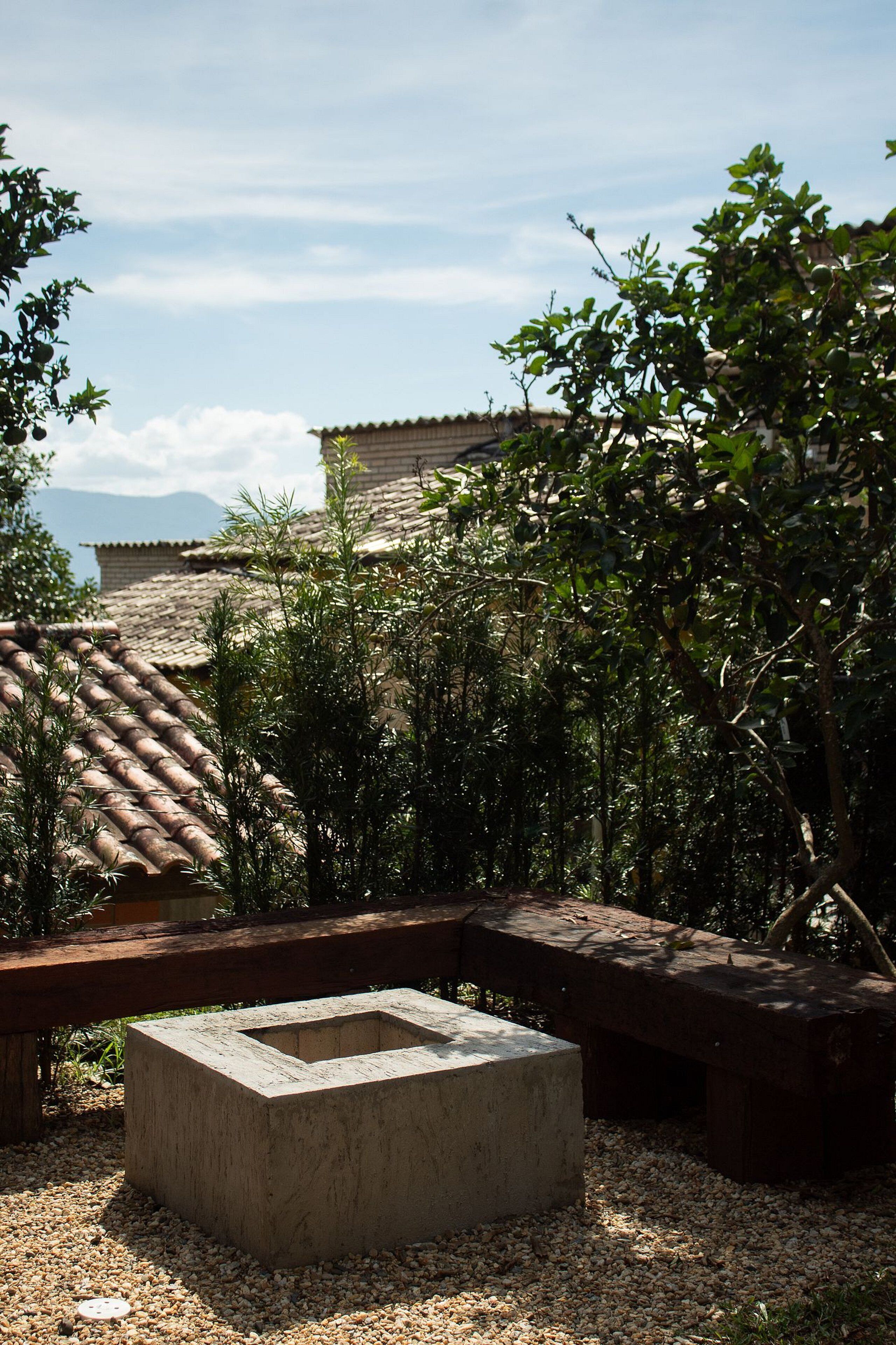 Une cour avec un bac à plantes en béton, un sol recouvert de gravier et une vue sur des toits couverts de tuiles en terre cuite.