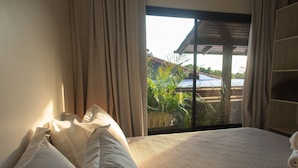 A bedroom with a large bed, a view of a garden through a sliding door, and a wooden ceiling structure. - Casas Valley Boutique - Praia do Rosa (Imbituba)