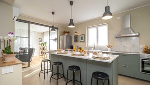 A modern kitchen with a central island, bar stools, pendant lighting, and a large window providing natural light. - Luxury Golf Villa in Bogogno (Bogogno)
