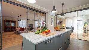 A modern kitchen with a marble countertop, a dining area with a table and chairs, and a living room with a sofa and a TV. - Luxury Golf Villa in Bogogno (Bogogno)