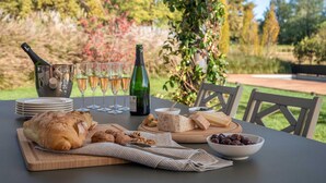 An outdoor dining setup with a table set for a meal, including bread, cheese, and olives, with wine glasses and a bottle. - Luxury Golf Villa in Bogogno (Bogogno)