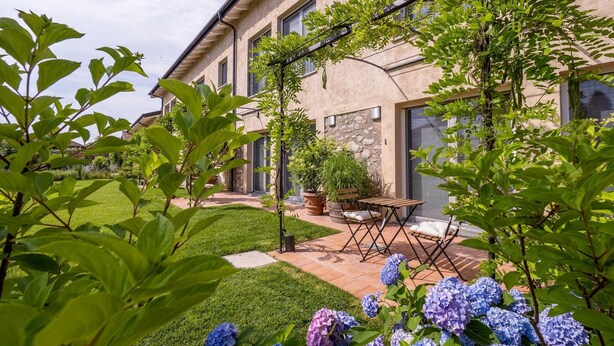 A building with a stone facade, a patio with a table and chairs, and a garden with hydrangea flowers. - Green Lodge - Apartment 1 - 1 BR 1 Bath (Cressa)