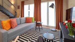 Una sala de estar con un sofá gris, un tapete a rayas negras y blancas, una mesita redonda y un jarrón con flores.