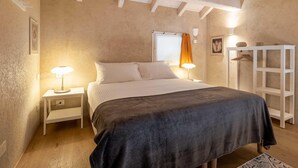 Un dormitorio con cama, mesitas de noche, un armario y una ventana con cortinas.