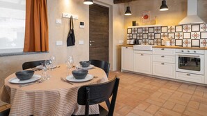 Un comedor con mantel a cuadros, sillas negras y una ventana con cortinas naranjas.