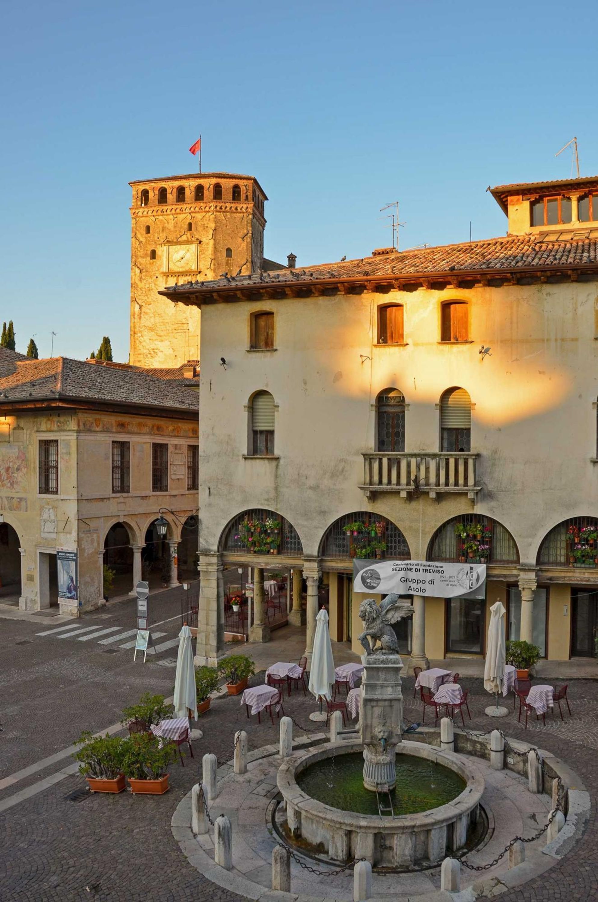 Un patio con una fuente, mobiliario exterior y un edificio histórico con una torre de reloj.