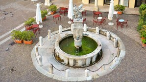 A circular fountain with a statue in the center, surrounded by potted plants and outdoor seating. - Palazzo Benassi Nobile (Asolo)