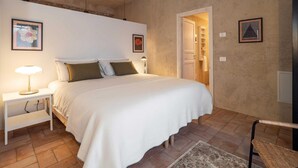 A bedroom with a large bed, bedside tables, a chair, and a door leading to a bathroom. - Green Lodge - Apartment 3 - 1 BR 1 Bath (Cressa)