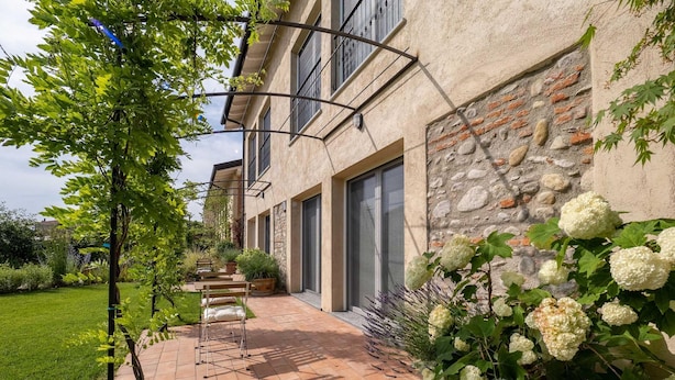 A modern building with a stone facade, a paved patio with outdoor furniture, and lush greenery. - Green Lodge - Apartment 3 - 1 BR 1 Bath (Cressa)