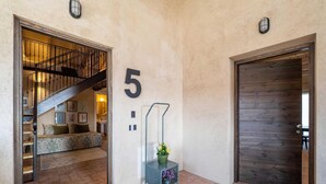 Un corridoio con una scala, una targa con il numero 5, un cancello in metallo e una porta in legno.