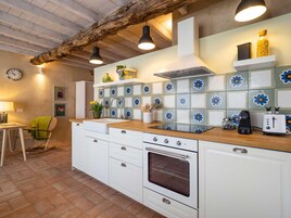 Una cocina con armarios blancos, encimera de madera, horno empotrado, un fregadero y salpicadero con baldosas azules y blancas.