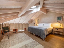 Un dormitorio acogedor en el ático con cama, una silla, un escritorio y un tragaluz.
