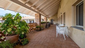 A covered patio area with brick flooring, potted plants, wicker furniture, and a brick pillar. - Green Lodge - Apartment 5 - 1 BR 1 Bath (Cressa)