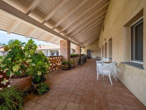 Un patio cubierto con suelo de ladrillo, plantas en macetas, muebles de mimbre y un pilar de ladrillo.