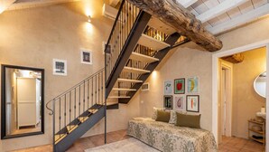 A bedroom with a staircase, a bed with a patterned bedspread, a rug, and framed pictures on the wall. - Green Lodge - Apartment 5 - 1 BR 1 Bath (Cressa)