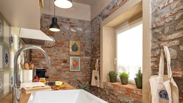 Een keuken met een grote witte spoelbak, een hanglamp en een bakstenen muur.