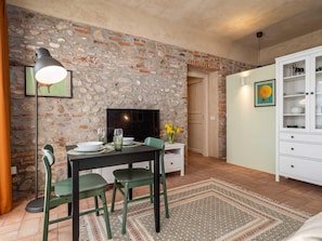A dining area with a stone wall, a TV, a cabinet, and a patterned rug. - Green Lodge - Apartment 2 - Studio (Cressa)