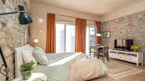 Een slaapkamer met een bed, een bureau, een televisie en een stenen muur.
