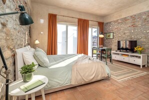 Un dormitorio con cama, escritorio, televisión y pared de piedra.