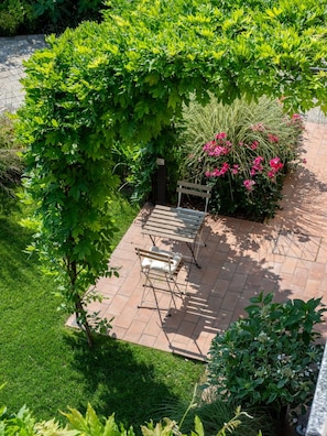 A patio area with a wooden bench and a table, surrounded by lush greenery and flowering plants. - Green Lodge - Apartment 2 - Studio (Cressa)