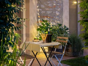 An outdoor dining area with a table set for two, surrounded by greenery and a stone wall. - Green Lodge - Apartment 2 - Studio (Cressa)