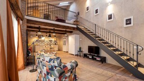 En rummelig opholdsstue med en stor sofa, en trappe og et køkken i baggrunden.