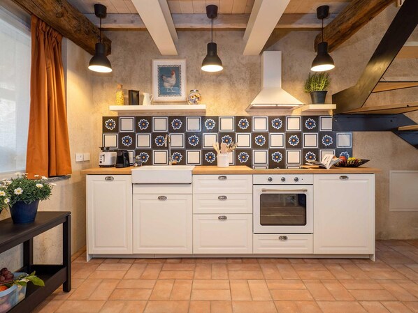 Une cuisine avec des armoires blanches, un four encastré, un pare-feu en carrelage, des luminaires suspendus et une fenêtre avec des rideaux.