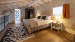 A bedroom with a bed, bedside tables, a window with curtains, a wooden ceiling, and a hallway leading to a bathroom. - Green Lodge - Apartment 7 - 2 BR 2 Bath (Cressa)