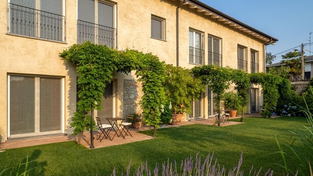 A two-story building with a garden, outdoor seating, and a stone wall. - Green Lodge - Apartment 7 - 2 BR 2 Bath (Cressa)