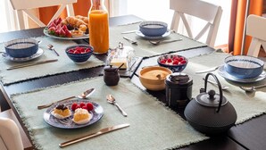 A breakfast setting with a table set for two, including plates with pastries, bowls of raspberries, a bottle of orange juice, and a teapot. - Green Lodge - Apartment 9 - 2 BR 1 Bath (Cressa)