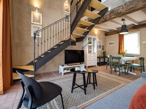 Un salon avec un escalier, un téléviseur, un coin repas et une fenêtre avec des rideaux.
