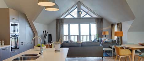 A modern kitchen with a central island, a dining area with a table and chairs, and a seating area with a sofa and cushions.