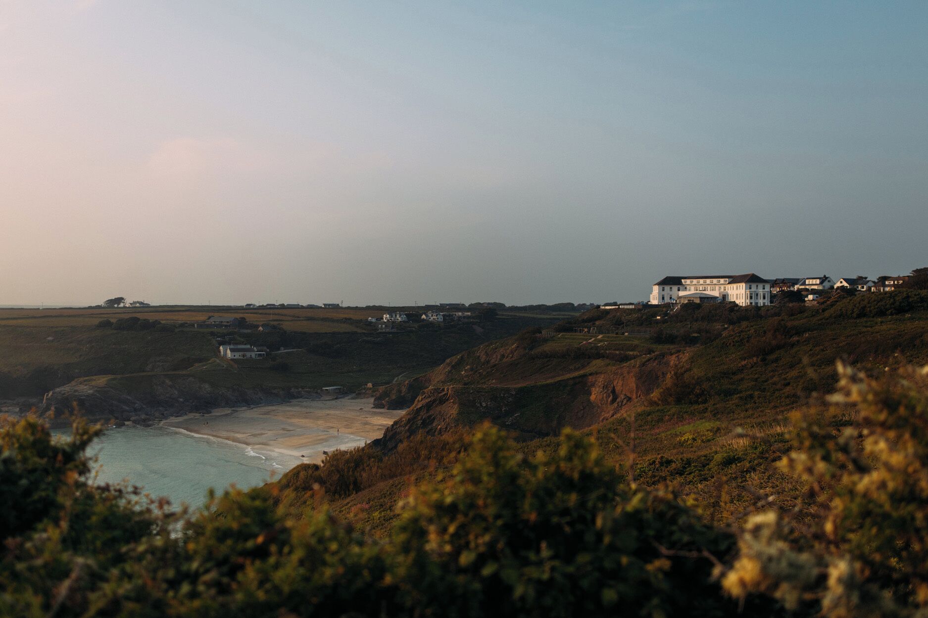 Un paysage côtier avec un imposant bâtiment blanc perché sur une colline, dominant une plage.