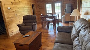 A wooden cabin interior with a sofa, armchair, dining table, and chairs.
