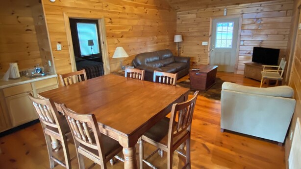 A wooden interior with a dining table, chairs, a sofa, a television, and a ceiling fan.