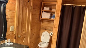 A wooden cabin bathroom with a sink, toilet, and shelves with towels.