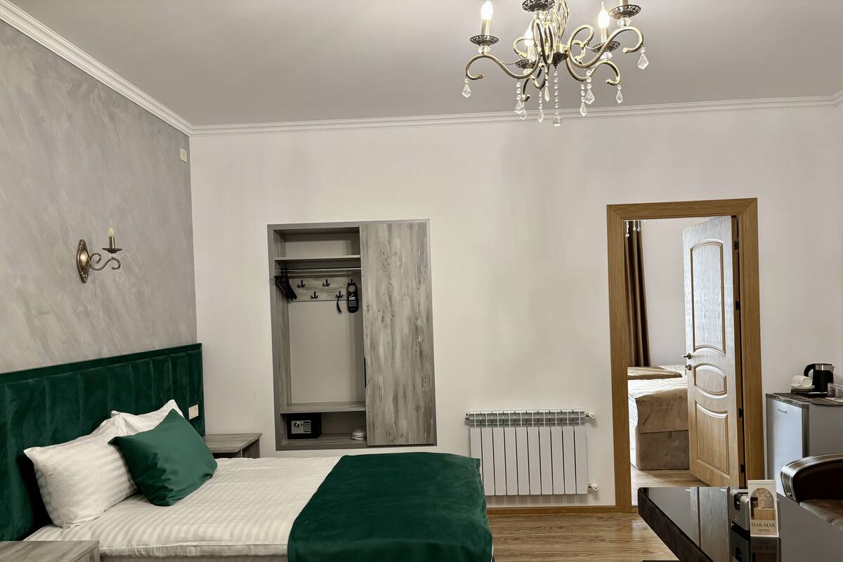 A hotel room with a bed, a vanity with a mirror, a radiator, and a door leading to another room.