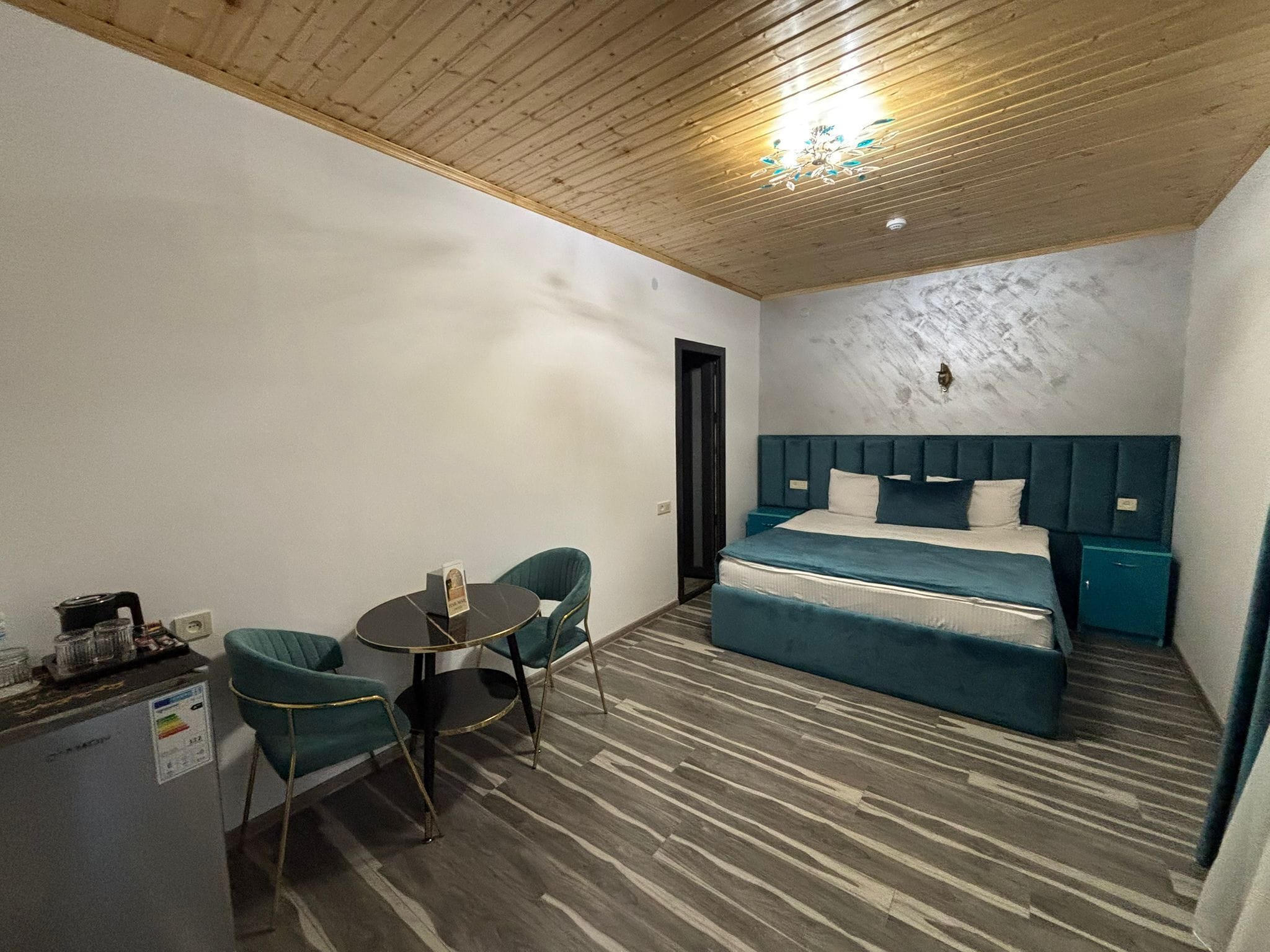 Una habitación con una cama, una pequeña mesa con sillas, una cafetera y techo de madera.